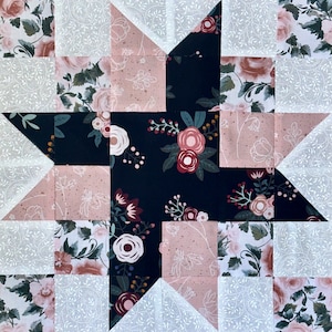 May include: A quilt block with a star design featuring a black fabric with pink and white floral print, a pink fabric with white floral print, and a white fabric with a gray floral print.