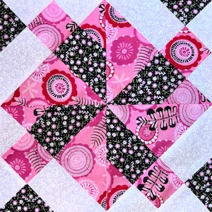 May include: A pink and black patchwork quilt block with a geometric design. The block is made up of squares and triangles, and the fabric has a floral pattern.
