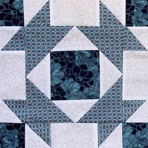 May include: A quilt block with a star pattern in shades of blue and white. The star is made up of triangles and squares, and the background is a white fabric with a subtle floral pattern.