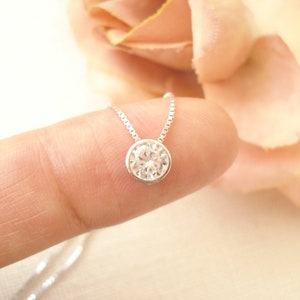 Puede incluir: Un delicado collar de cadena de plata con un solo colgante redondo de cristal transparente.