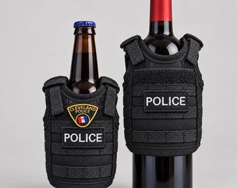 Peut inclure: Deux housses de bouteille en forme de gilet tactique noir conçues pour s'adapter aux contenants. La plus petite housse porte un écusson Cleveland Police et une étiquette Police. La plus grande porte une étiquette Police. Sangles incluses.
