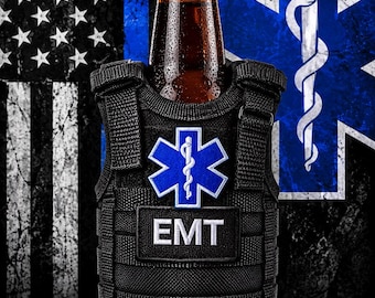 May include: A black tactical vest beverage cooler featuring a blue Star of Life emblem and a rectangular patch with the white text EMT. The vest is wrapped around a brown glass bottle with a red cap, displaying a textured, modular webbing design.