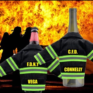 May include: Two wine bottle covers shaped like firefighter jackets. The jacket on the left is black with yellow reflective stripes and says "F.D.N.Y. VEGA". The jacket on the right is black with yellow reflective stripes and says "C.F.D. CONNELLY".