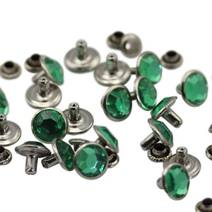 May include: A collection of silver-toned metal rivets with faceted emerald green glass stones. The rivets have a post and cap design, with small, matching metal washers. The gemstones are oval and round.