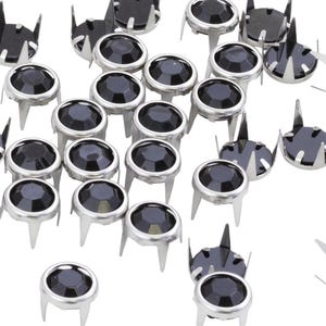 May include: A collection of silver-colored metal studs with black, faceted, jewel-like centers. The studs have three or four pointed prongs and are scattered against a white background. These decorative studs are ideal for adding embellishments to clothing or accessories.