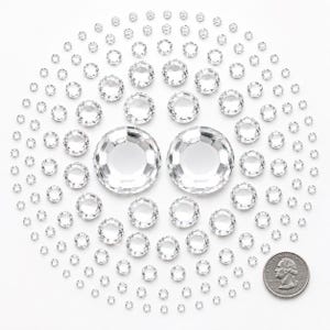 May include: A collection of clear, faceted circular rhinestones arranged in a circular pattern, varying in size from small to large. A United States quarter coin is placed in the lower right corner to provide a scale reference for the crystals.