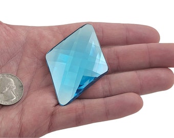 May include: A large, light blue, faceted, diamond-shaped crystal. The crystal is about the size of a US quarter.