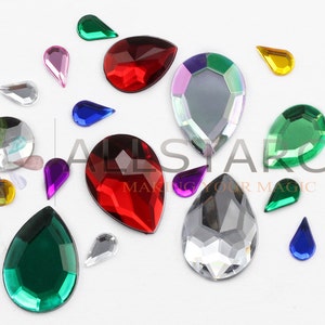 May include: Assortment of teardrop-shaped rhinestones in various colors, including red, green, purple, blue, and clear. The rhinestones vary in size and are scattered across a white surface. The image includes the text "ALLSTARCO MAKING YOUR MAGIC."