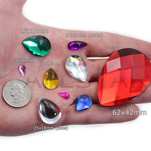 May include: Assorted teardrop-shaped gemstones in various colors, including green, purple, yellow, iridescent, pink, blue, and red. Sizes range from 10x6mm to 62x42mm. A US quarter is included for size comparison.