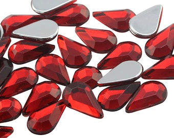 May include: A group of red teardrop-shaped rhinestones. The rhinestones have a faceted design and are scattered on a white background.