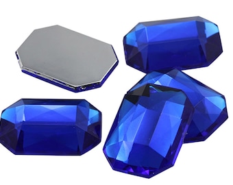May include: Five blue, faceted, rectangular glass gems. The gems are arranged in a cluster on a white background.