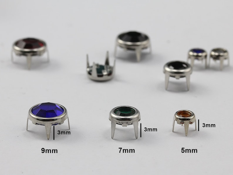 May include: A collection of gemstone rivets in various colors, including red, black, blue, green, and amber. The rivets have a silver-colored metal base with three prongs and are 5mm, 7mm, and 9mm in diameter.