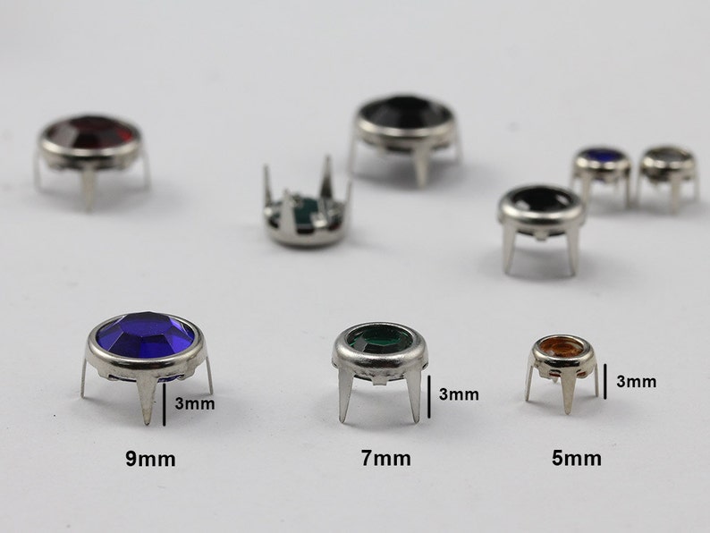 May include: A selection of gemstone rivets in various colours, including red, black, blue, green, and amber. The rivets have a silver-coloured metal base with three prongs and are 5mm, 7mm, and 9mm in diameter.