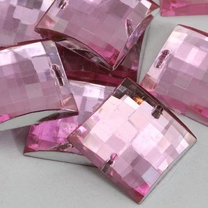 May include: A group of pink, faceted, square-shaped glass rhinestones with a slight curve. The rhinestones have a silver backing.