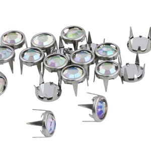 May include: A collection of silver-toned metal studs with iridescent, faceted, round crystal centers. Each stud has a pointed post and four prongs to secure the crystal. The studs are scattered against a white background.