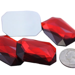 Puede incluir: Cuatro gemas de vidrio rectangulares rojas facetadas. Las gemas están dispuestas en una fila, con las dos de los extremos superponiéndose ligeramente a las dos del medio. Las gemas tienen aproximadamente el tamaño de una moneda de euro.