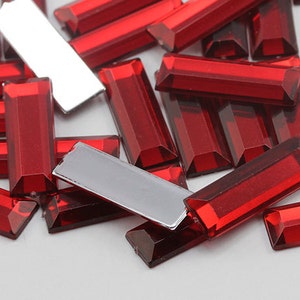 May include: A pile of red rectangular glass rhinestones. The rhinestones are faceted and have a shiny finish.