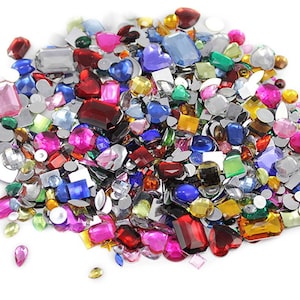 Pode incluir: Uma coleção de strass coloridos em várias formas e tamanhos, incluindo corações, quadrados e ovais. As pedras preciosas são em tons de vermelho, rosa, azul, verde e amarelo, com acabamentos transparentes e iridescentes. Ideal para artesanato e embelezamento.