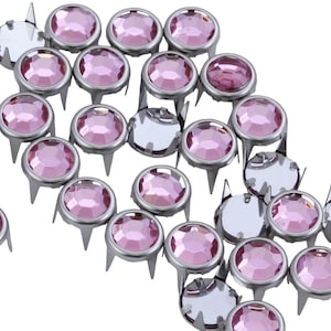 May include: A scattering of pink rhinestones with silver settings and prongs. The rhinestones are arranged in a random pattern on a white background.