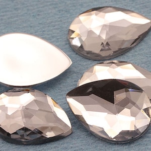 May include: Five clear teardrop-shaped glass rhinestones with a faceted design. The rhinestones are on a blue surface.