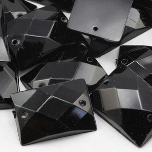 May include: A collection of faceted black glass beads. The beads have a geometric design with multiple flat surfaces and a hole for stringing. The beads are rectangular and diamond-shaped.