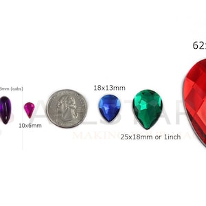 May include: Assortment of teardrop-shaped gemstones in various colors and sizes. Includes clear, purple, pink, blue, and green stones, with a large red faceted stone measuring 62x42mm. Sizes range from 10x6mm to 25x18mm (cabs) or 1 inch.