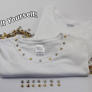 May include: Two white t-shirts, one folded and embellished with silver and gold star and round studs around the neckline. Scattered studs in various shapes and colors are displayed. The text "Do It Yourself!" is in the upper left corner.