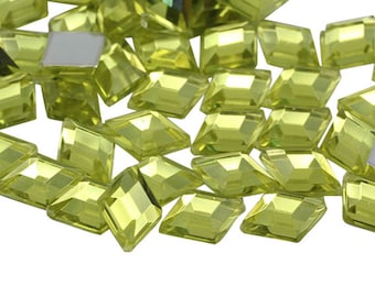 May include: A scattering of light green, faceted, rectangular rhinestones. The rhinestones have a slightly rounded edge and are scattered on a white background.