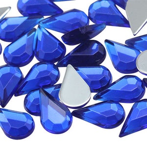 May include: A collection of blue teardrop-shaped rhinestones. The rhinestones are faceted and have a shiny finish.