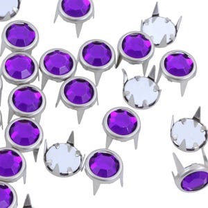 May include: Close-up of scattered silver-colored metal studs with purple faceted gems. The studs have a round gem set in a metal base with three prongs. The gems are a vibrant purple color.
