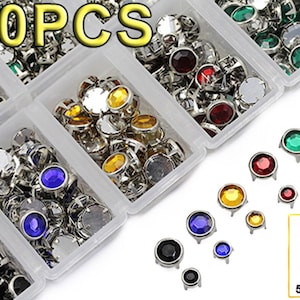 May include: A collection of 900 assorted gemstone rivets in a clear plastic organizer. The rivets feature various colors, including clear, red, green, yellow, blue, and black. Sizes are 5mm and 7mm.