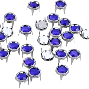 May include: A collection of blue rhinestone nailheads with silver bases. The nailheads are scattered on a white background.