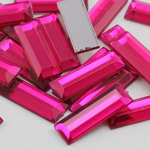 May include: A large quantity of bright pink rectangular glass rhinestones. The rhinestones have a faceted, reflective surface.