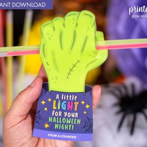 Puede incluir: Un soporte para bastón luminoso impreso en forma de mano de monstruo verde con una tarjeta morada y azul que dice "A little LIGHT for your HALLOWEEN NIGHT! From Alexander".