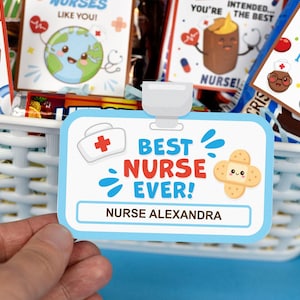 Puede incluir: Una tarjeta azul y blanca con el texto "Best Nurse Ever!" y el nombre "Nurse Alexandra". La tarjeta est&aacute; decorada con una cruz roja, una venda con una cara sonriente y remolinos azules y blancos.