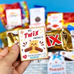 Puede incluir: Una barra de chocolate Twix envuelta en papel dorado con una tarjeta que dice "No Twix About It. You're the Best Nurse!" La tarjeta tiene una barra de Twix de dibujos animados con un gorro de enfermera y una cara sonriente.