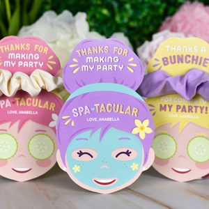 K&ouml;nnte beinhalten: Drei Partygeschenke zum Thema Spa mit Scrunchies. Jedes Geschenk zeigt ein Cartoon-Gesicht mit Gurken-Augenmasken und dem Text "Danke, dass du meine Party gemacht hast" und "Spa-Tacular". Farben sind Pink, Lila und Gelb.