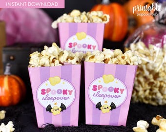 May include: Printable popcorn boxes with a pink and purple striped design. The boxes feature a cute cartoon bat and the text "Spooky Sleepover".