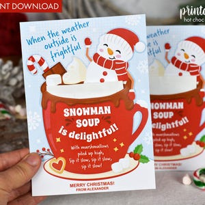 Puede incluir: Una tarjeta de Navidad imprimible con un mu&ntilde;eco de nieve en una taza roja con chocolate caliente y malvaviscos. La tarjeta dice "Cuando el clima afuera es espantoso, &iexcl;la sopa de mu&ntilde;eco de nieve es deliciosa!" con un mensaje festivo en la parte inferior.