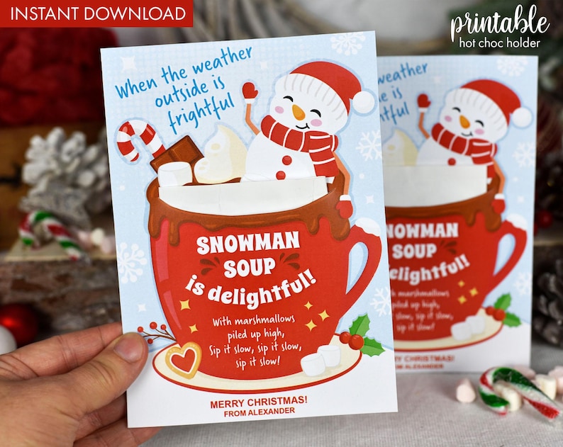 Puede incluir: Una tarjeta de Navidad imprimible con un mu&ntilde;eco de nieve en una taza roja con chocolate caliente y malvaviscos. La tarjeta dice "Cuando el clima afuera es espantoso, &iexcl;la sopa de mu&ntilde;eco de nieve es deliciosa!" con un mensaje festivo en la parte inferior.