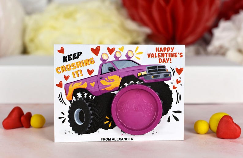 May include: A Valentine's Day card featuring a cartoon monster truck with the text "Keep Crushing It!" and "Happy Valentine's Day!"  The card includes a pink play dough container with the word "Play-Doh" printed on it. The card is signed "From Alexander."
