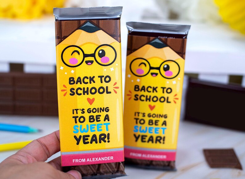 Op de afbeelding: Twee chocoladerepen met gele verpakkingen met een potloodontwerp en de tekst "Back to School". De verpakkingen zeggen ook "It's going to be a sweet year!" en "From Alexander".