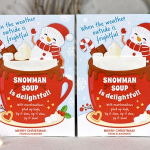 Puede incluir: Dos tarjetas de Navidad con un mu&ntilde;eco de nieve en una taza roja de chocolate caliente con malvaviscos. El texto de la tarjeta dice "Cuando el clima afuera es espantoso, &iexcl;la sopa de mu&ntilde;eco de nieve es deliciosa!" con malvaviscos apilados alto, b&eacute;belo despacio, b&eacute;belo despacio, b&eacute;belo despacio! &iexcl;Feliz Navidad! De parte de Alexander.