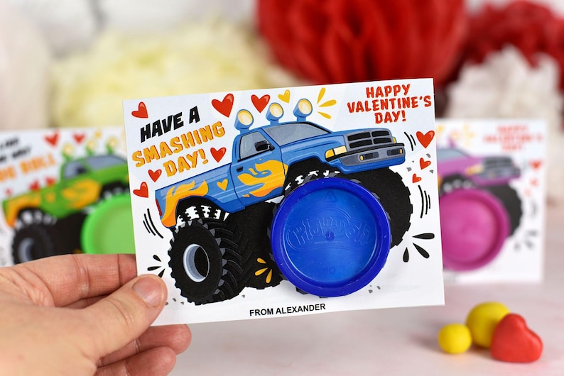 May include: A blue monster truck with yellow flames on the side, a blue Play-Doh container, and a Valentine's Day card that says "Have a Smashing Day!" and "Happy Valentine's Day!" The card is signed "From Alexander."