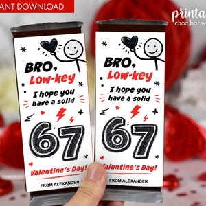 Könnte beinhalten: Zwei Schokoriegelverpackungen mit Valentinsthema. Die Verpackungen zeigen den Text "BRO, Low-key" und "I hope you have a solid 67 Valentine's Day!" mit einer Strichmännchenfigur, die ein Herz hält.