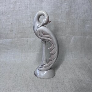 May include: A ceramic swan figurine in shades of gray and lavender. The swan has a curved neck and detailed feather design. The figurine stands on a round base and is a decorative item.