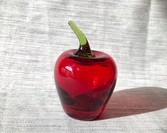 May include: A vibrant red glass apple sculpture with a green stem. The apple is smooth and glossy, reflecting light. This decorative piece adds a pop of color and is a unique home decor item.