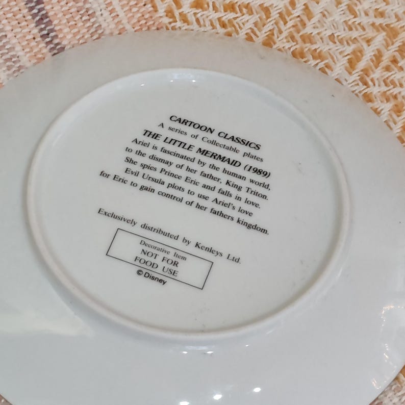 Puede incluir: Un plato de cer&aacute;mica blanco con texto de la pel&iacute;cula animada de Disney "La Sirenita" (1989). El plato incluye texto sobre Ariel, el Rey Trit&oacute;n, el Pr&iacute;ncipe Eric y &Uacute;rsula. Es un art&iacute;culo decorativo, no apto para uso alimentario.