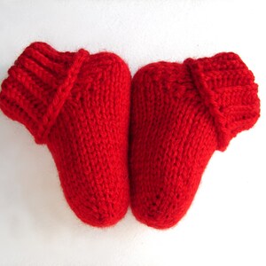 Può includere: Un paio di scarpine per neonati in maglia rossa con un risvolto piegato. Le scarpine sono realizzate in un filato morbido e caldo, perfette per mantenere le piccole dita dei piedi al caldo.