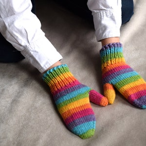 Rainbow colored wool mittens presented on child's hands. Rainbow stripes are mismatched on the two mittens. Color progression is: green, blue, purple, magenta, orange, yellow repeating.